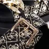 A close-up view of a black sandal with a gold buckle and a patterned fabric strap. Podgląd zdjęcia produktu