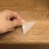 A hand is peeling a transparent, self-adhesive anti-slip film from a wooden surface. Produktbild-Vorschau