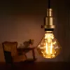 A diamond-shaped LED light bulb with a gold-colored socket hangs in the foreground, with a blurred antique armchair and table in the background. Anteprima dell’immagine prodotto