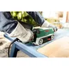 A person wearing gloves is using a Bosch belt sander on a blue table outdoors. Podgląd zdjęcia produktu
