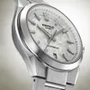 Close-up of a silver analog watch with a white textured dial. Produktbild-Vorschau