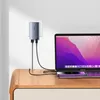 A gray Baseus GaN5 Pro Fast 65W USB-C USB-A charger is plugged into a wall socket and connected via USB-C cables to a MacBook Pro and an iPhone, all placed on a wooden desk. Náhľad obrázku produktu