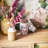 A collection of colored pencils in a decorative container, alongside two vases with dried flowers, displayed on a wooden surface with books. Produktbild-Vorschau