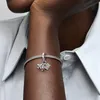 A close-up shot of a person's arm wearing a Pandora Moments charm bracelet with a plane, globe, and suitcase charm. Podgląd zdjęcia produktu