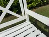 A close-up view of a white wooden garden bench with green foliage in the background. Produktbild-Vorschau
