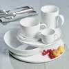 A set of white ceramic dishes and cutlery on a light gray tablecloth. Produktbild-Vorschau