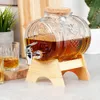 A glass beverage dispenser filled with amber liquid, sitting on a wooden stand, with a glass and a shot glass nearby. Produktbild-Vorschau