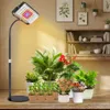 A grow lamp illuminates several potted plants on a wooden surface, with a bookshelf in the background. Produktbild-Vorschau