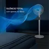 A white standing fan is shown in a bedroom setting, with a blue wave graphic emanating from it, representing airflow and silence. Voir les images du produit