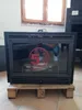 A fireplace insert is placed on a wooden pallet in front of a window. Náhled obrázku produktu