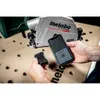 A person is holding a small black tracker device and a smartphone displaying a map application, with a Metabo power tool in the background. Voir les images du produit