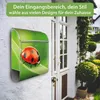 A mailbox with a ladybug design is mounted on a white brick wall next to a white door, with greenery in the background. Produktbild-Vorschau