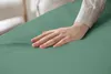 A hand is touching a light green fabric, likely a bedsheet. Produktbild-Vorschau