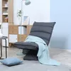 A dark gray floor sofa with a light blue blanket draped over it, placed in a living room setting with a bookshelf and a floor lamp. Náhled obrázku produktu