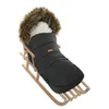 A black winter footmuff with a fur-lined hood is placed on a wooden sled. Podgląd zdjęcia produktu