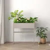A modern planter with plants and flowers on a wooden floor next to a curtain. Voir les images du produit