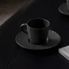 A black coffee cup and saucer on a black wooden table. Produktbild-Vorschau