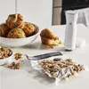 A kitchen counter scene with muffins, walnuts, a vacuum sealer, and a vacuum-sealed bag of walnuts. Náhľad obrázku produktu