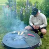 A person is grilling food on a large fire pit in a garden with flowers. Anteprima dell’immagine prodotto