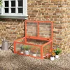 A wooden cold frame greenhouse with a clear polycarbonate lid is placed on gravel next to a brick wall and a window. Produktbild-Vorschau