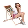 A woman sitting on a folding deck chair with a vintage garage-themed print. Náhľad obrázku produktu