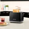 A black Russell Hobbs toaster with two slices of toast in it, placed on a kitchen counter next to a jar of jam and a slice of toast with jam. Podgląd zdjęcia produktu