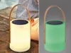 Two images of a solar lantern, one lit white and the other lit green, placed on a wooden surface. Produktbild-Vorschau