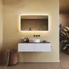 A modern bathroom vanity with a backlit mirror, sink, and storage. A laundry basket and plant are also visible. Náhled obrázku produktu