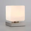 A modern cube-shaped table lamp with a brushed metal base. Anteprima dell’immagine prodotto