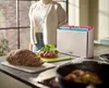 A kitchen scene with a person in the background, a sliced roast, radishes, and a cutting board set. Podgląd zdjęcia produktu