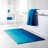 A blue gradient bath mat is placed on a white floor in front of a white bathtub. Two blue towels are draped over the edge of the bathtub. Podgląd zdjęcia produktu