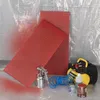 A painting setup with red perforated panels, a spray gun, an air compressor, and paint cans. Produktbild-Vorschau