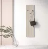 A wall-mounted coat rack with a purse hanging from it, next to a vase with greenery. Produktbild-Vorschau