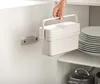 A hand is holding a white compost bin over a shelf with plates and pots. Náhled obrázku produktu
