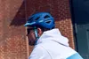 A man wearing a blue bicycle helmet and a white hoodie, seen from the side. Náhľad obrázku produktu
