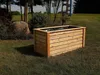 A wooden planter box sits on a grassy lawn in a garden setting, with trees and bushes in the background. Produktbild-Vorschau
