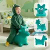 A young child in a dinosaur costume is happily riding a green inflatable dinosaur toy in a bedroom decorated with dinosaur-themed wallpaper and bedding. Podgląd zdjęcia produktu