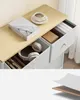 A close-up view of a light-colored storage unit with drawers, featuring a book, a cup of coffee, and headphones. Náhled obrázku produktu