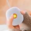 A person's hands holding a white, pebble-shaped device with a glowing orange light in the center. Podgląd zdjęcia produktu