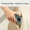 A hand is holding a small green digital camera and placing it into a pocket of a beige garment. Produktbild-Vorschau