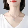 A close-up shot of a person wearing a silver heart-shaped pendant necklace. Anteprima dell’immagine prodotto