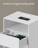 A white nightstand with a drawer and an open shelf, featuring a smartphone charging on top and glasses and a tablet inside the drawer. Produktbild-Vorschau