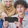Two young people are looking at a smartphone held horizontally by the person in the foreground. Podgląd zdjęcia produktu