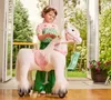 A young girl in a princess-like dress is brushing the mane of a white toy horse with a pink saddle. The scene is set in a bright, airy room with large glass doors opening to a backyard with a slide and flowers. Anteprima dell’immagine prodotto