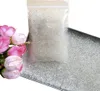 A bag of clear beads and a tray filled with the same beads, with a bouquet of pink and white flowers to the left. Produktbild-Vorschau
