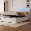 A white upholstered bed with a lifted mattress, revealing storage space underneath. The headboard has blue LED lighting. Náhled obrázku produktu