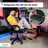 A man is sitting in a gaming chair, talking on the phone, with his feet resting on a footrest. The background shows a gaming setup with computers and neon lights. Produktbild-Vorschau