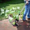 A person is using a foldable trolley to move a potted plant on a brick pathway. Náhled obrázku produktu