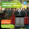 A gas cylinder system with two red gas bottles connected to a silver central unit, set against a blurred background of plants and greenery. Produktbild-Vorschau