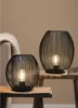 Two black wire frame lanterns with light bulbs inside are placed on wooden surfaces. Anteprima dell’immagine prodotto